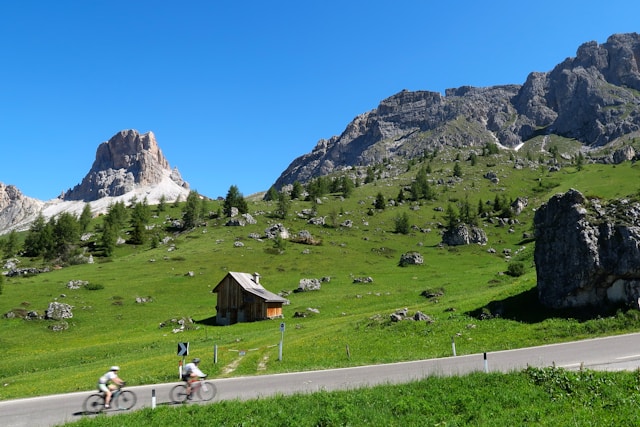 scene of the dolomite mountain and green field with two people on bikes cycling in italy