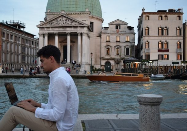 man working on a laptop in front of Venice's canals, taking advantage of the new italy digital nomad visa