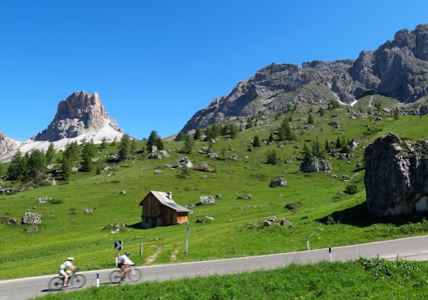 scene of the dolomite mountain and green field with two people on bikes cycling in italy